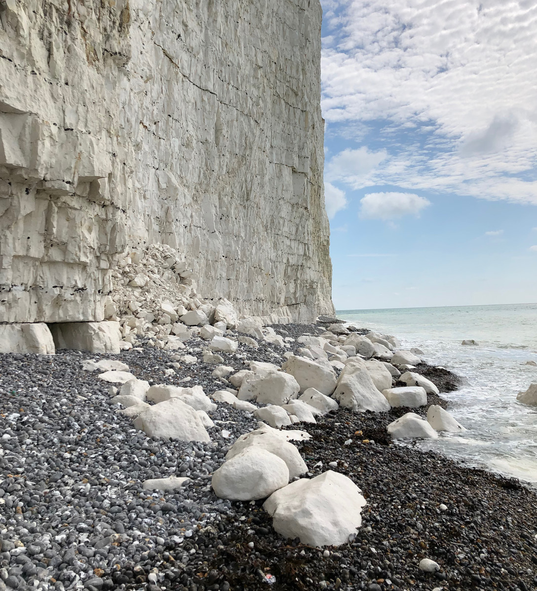 Looking from the beach at some white cliffs along the coast of the English Channel with large white boulders of chalk that have fallen on to a beach of grey pebbles