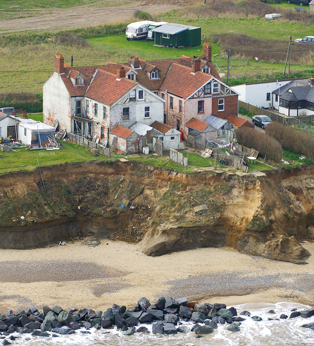 Several houses only a few metres away from the edge of a cliff with gardens that have collapsed in to the sea due to coastal erosion.